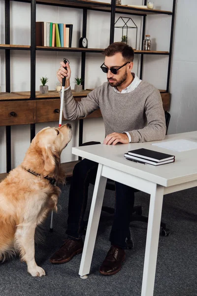 Blind man sitting at table beside golden retriever at home — Stock Photo