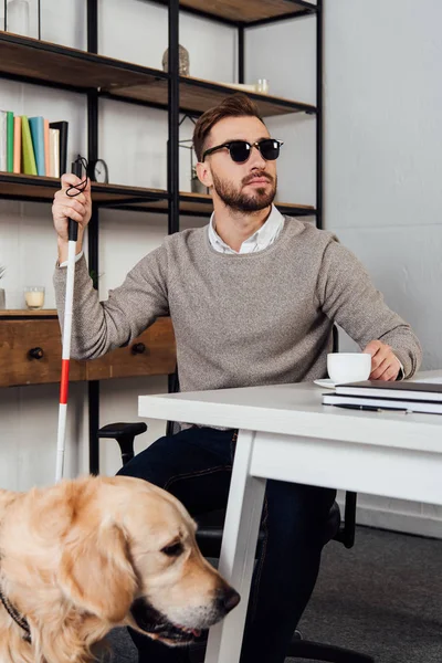Blind man drinking coffee at table beside golden retriever — Stock Photo