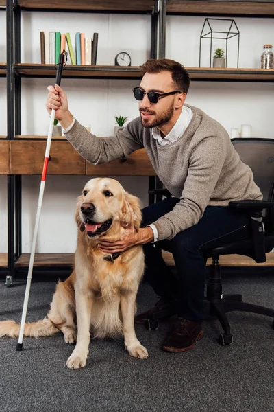 Blind man with walking stick petting golden retriever at home — Stock Photo