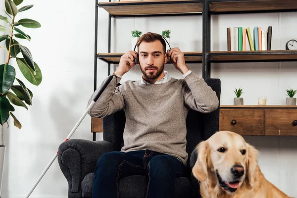 Homme malvoyant utilisant un casque à côté de golden retriever à la maison — Photo de stock