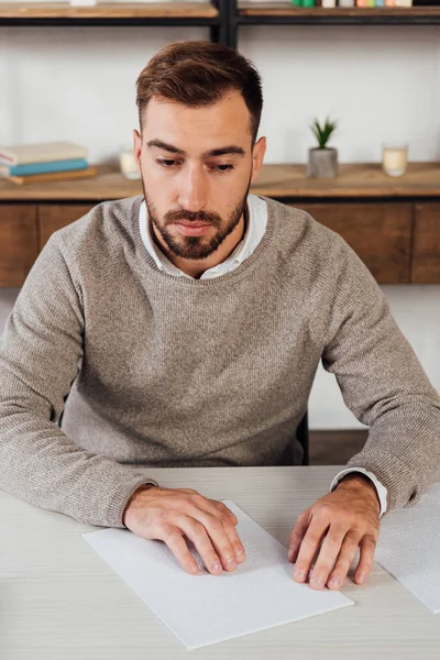 Blind man reading paper with braille font at table — Stock Photo