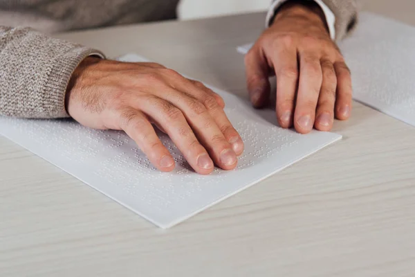 Cropped view of bind man reading braille font on paper at table — Stock Photo