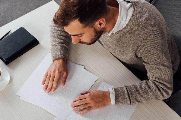 Vista ad alto angolo su un uomo ipovedente che legge il carattere braille a tavola — Foto stock