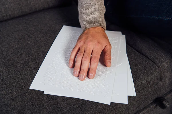 Cropped view of blind man reading braille font on sofa — Stock Photo