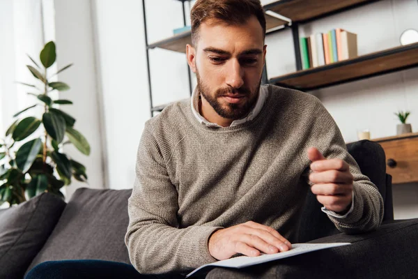 Visually impaired man reading braille font on sofa in living room — Stock Photo