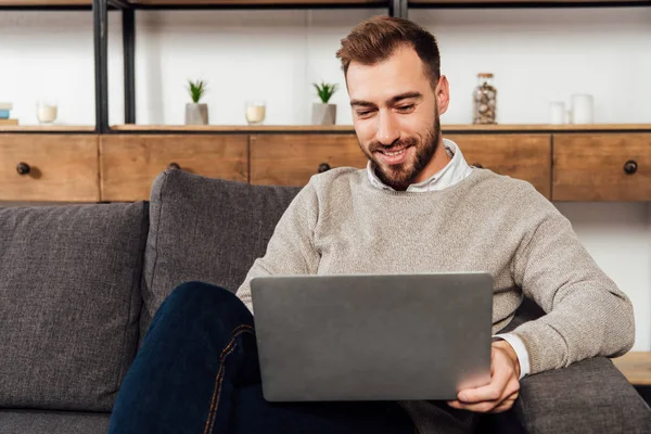 Homme souriant utilisant un ordinateur portable sur le canapé dans le salon — Photo de stock