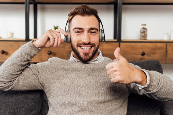 Hombre con auriculares sonriendo a la cámara y mostrando el gesto de pulgar hacia arriba - foto de stock