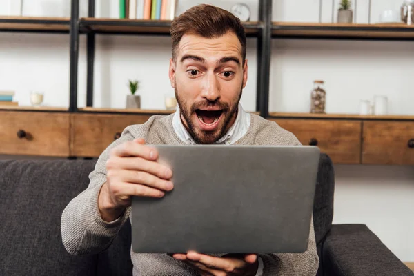 Exited man holding laptop on sofa in living room — Stock Photo