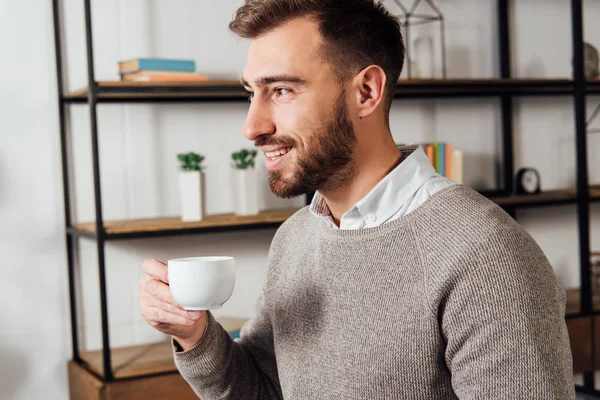 Sorrindo homem bonito bebendo café e olhando para longe em casa — Fotografia de Stock