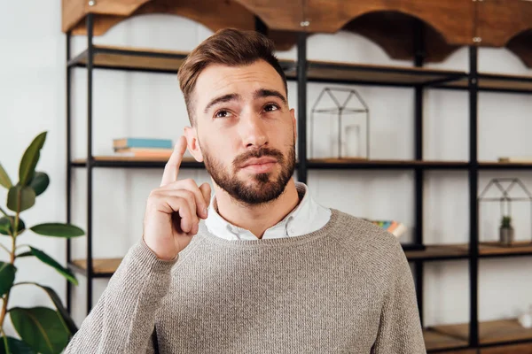 Nachdenklicher Mann zeigt zu Hause mit dem Finger nach oben — Stockfoto