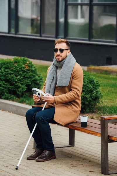 Blind man holding headphones while sitting on bench — Stock Photo