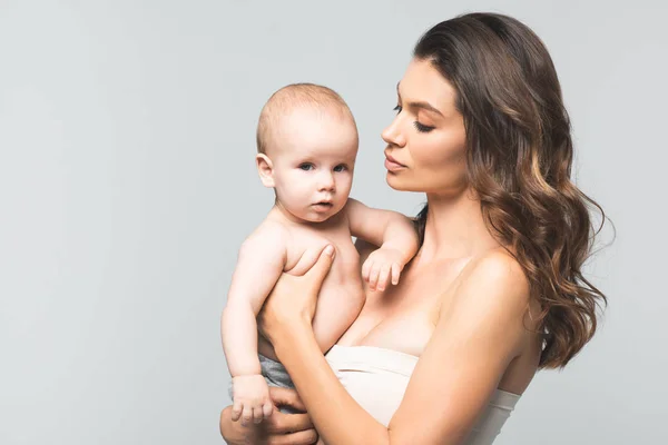 Retrato de madre atractiva sosteniendo bebé niño, aislado en gris - foto de stock