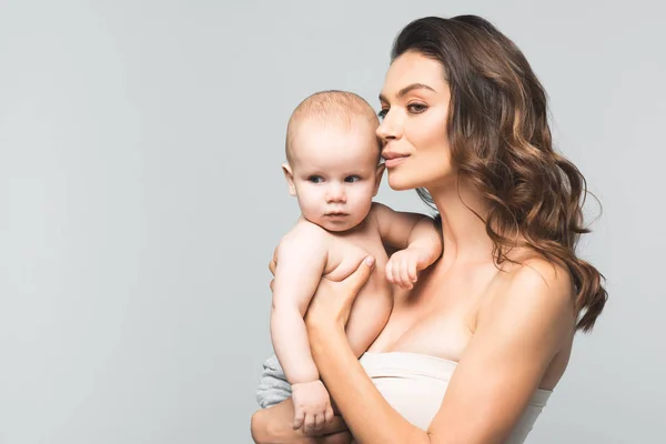 Ritratto di una bella madre felice che tiene in braccio un bambino adorabile, isolato sul grigio — Foto stock