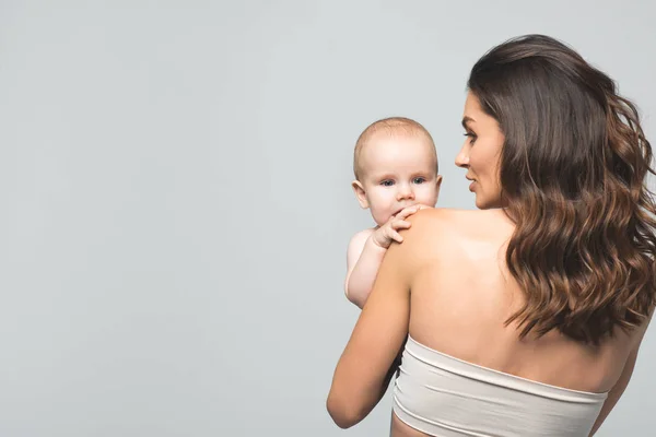 Rückseite der attraktiven Mutter, die einen kleinen Jungen hält, isoliert auf grau — Stockfoto