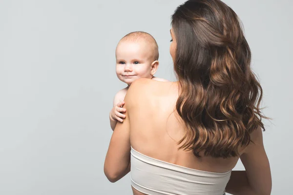 Vue de dos de la jeune mère tenant bébé garçon, isolé sur gris — Photo de stock