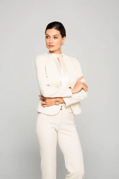 Елегантна впевнена бізнес-леді в білому костюмі з схрещеними руками, ізольована на сірому — стокове фото
