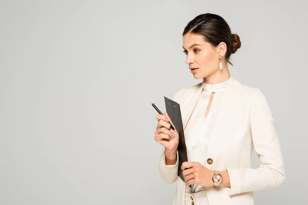 Красива бізнес-леді в білому костюмі тримає кишеню і ручку, ізольована на сірому — стокове фото