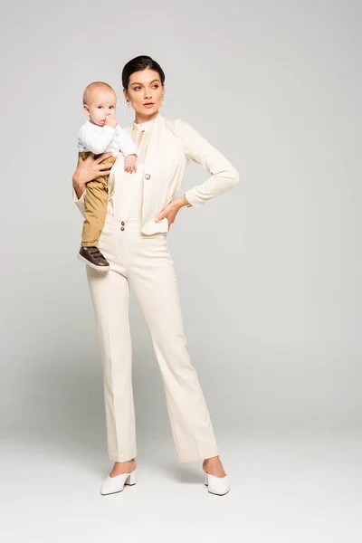 Jolie femme d'affaires tenant petit bébé sur les mains, sur gris — Photo de stock