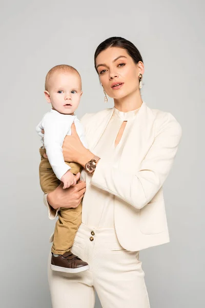 Beautiful businesswoman with adorable baby on hands, isolated on grey — Stock Photo