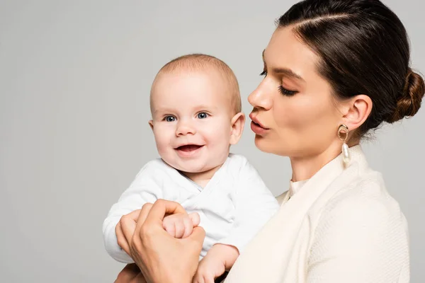 Hermosa mujer de negocios hablando con pequeño bebé sonriente, aislado en gris - foto de stock