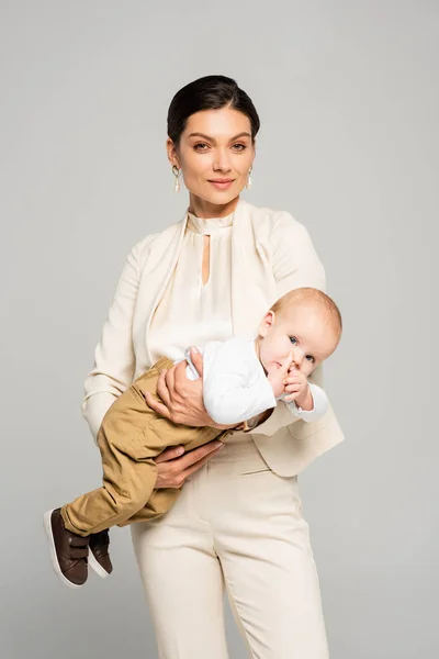 Bela mulher de negócios positiva com pouco bebê a mãos, isolado em cinza — Fotografia de Stock