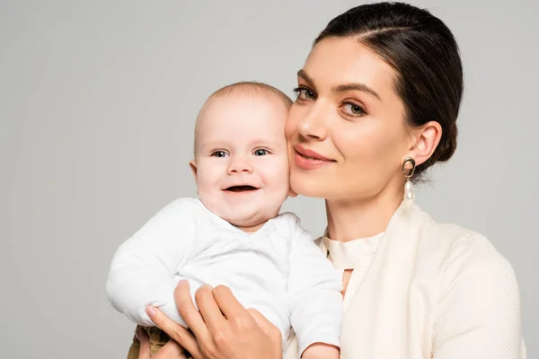 Cheerful businesswoman with smiling baby on hands, isolated on grey — Stock Photo