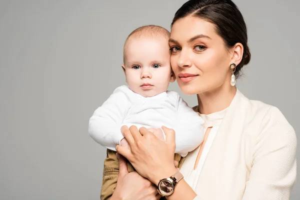 Lächelnde Geschäftsfrau mit kleinem Baby an den Händen, isoliert auf grau — Stockfoto