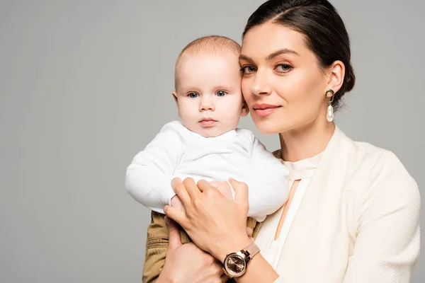 Femme d'affaires souriante avec petit bébé sur les mains, isolée sur le gris — Photo de stock