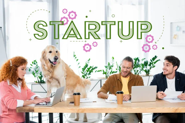 Three friends smiling and doing paperwork, golden retriever sitting on table in office with startup illustration — Stock Photo