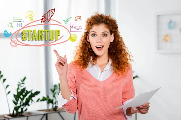Attraktive und schockierte Geschäftsfrau zeigt Ideenschild und hält Papier mit Startup-Illustration in der Hand — Stockfoto