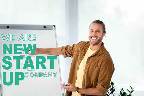 Handsome and smiling businessman pointing at flipchart with we are new startup company illustration — Stock Photo