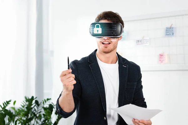 Businessman in shirt with virtual reality headset with cyber security illustration holding pen and papers — Stock Photo