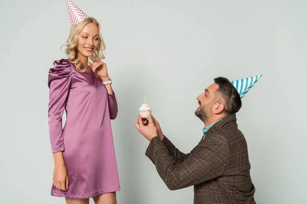 Fröhlicher Mann überreicht Geburtstagstorte an attraktive Frau auf grauem Hintergrund — Stockfoto