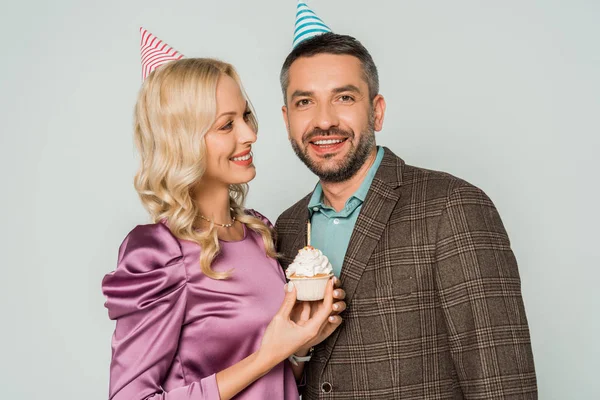 Donna sorridente con compleanno cupcake guardando felice marito isolato su grigio — Foto stock