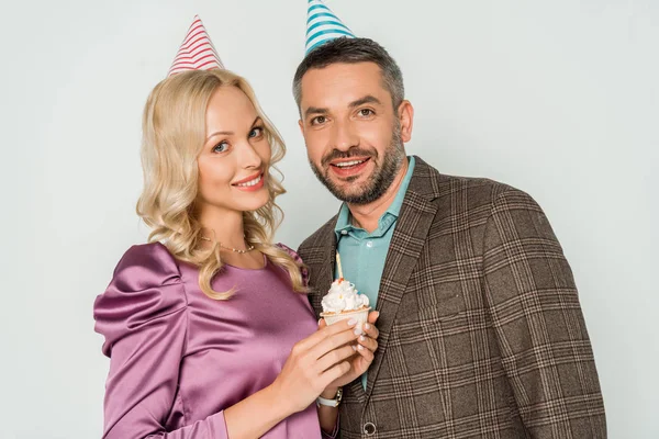 Donna attraente con cupcake di compleanno, e marito sorridente guardando la fotocamera isolata su grigio — Foto stock