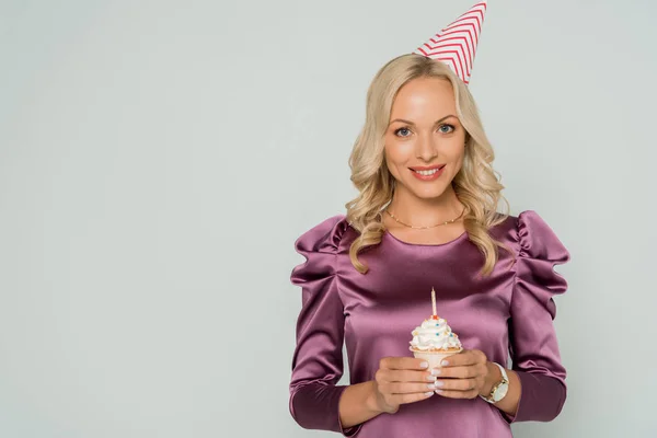 Feliz, mujer elegante en la tapa del partido celebración cupcake cumpleaños y sonriendo a la cámara aislada en gris - foto de stock