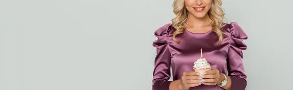 Cropped view of smiling woman holding cupcake with candle isolated on grey, panoramic shot — Stock Photo