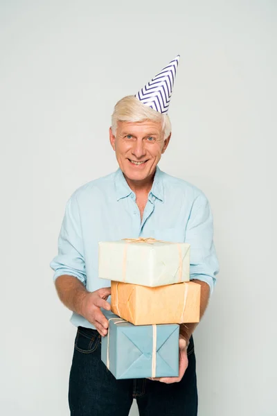 Happy senior man holding gift boxes while smiling at camera isolated on grey — Stock Photo