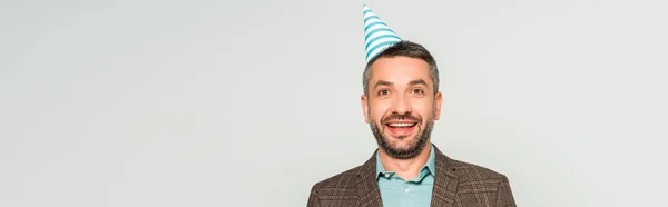 Panoramic shot of happy man in party cap looking at camera isolated on grey — Stock Photo