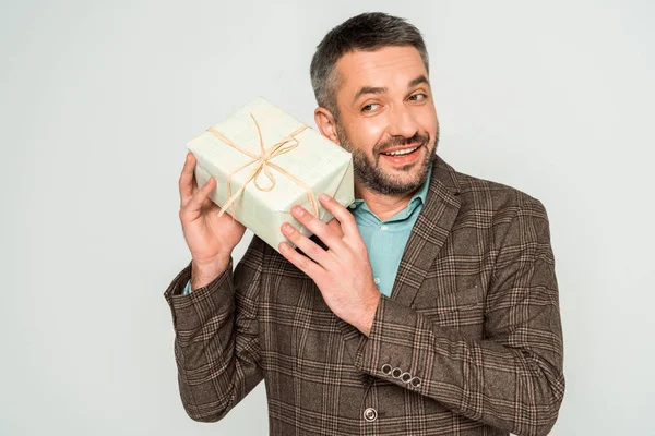 Lächelnder, neugieriger Mann schüttelt Geschenkbox isoliert auf grau — Stockfoto