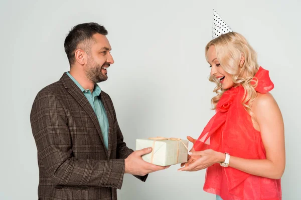 Усміхнений чоловік представляє подарункову коробку щасливій дружині на сірому фоні — стокове фото