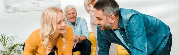 Panoramic shot of cheerful man and woman playing twister game near adult daughter and son sitting on sofa — Stock Photo
