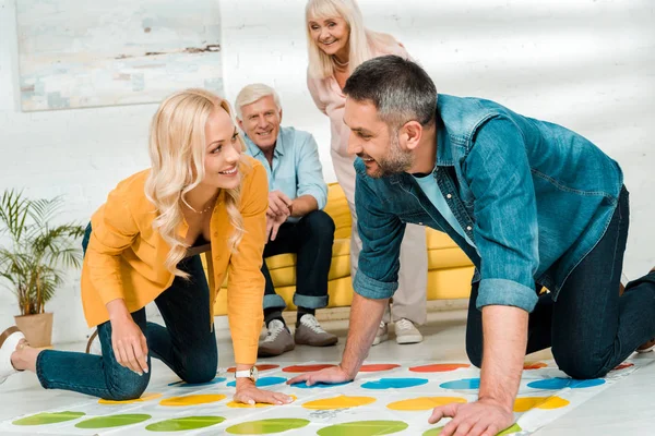 KYIV, UKRAINE - 21 NOVEMBRE 2019 : homme et femme joyeux jouant à twister game près de parents âgés assis sur le canapé — Photo de stock