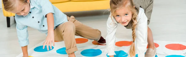 KYIV, UKRAINE - NOVEMBER 21, 2019: panoramic shot of cheerful kids playing twister game on floor at home — Stock Photo