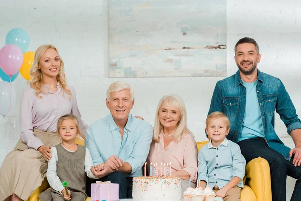 Família feliz sentado perto de bolo de aniversário e olhando para a câmera — Fotografia de Stock