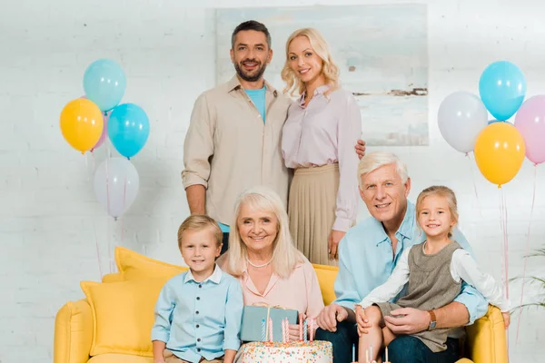 Família feliz olhando para a câmera perto de bolo de aniversário e balões festivos coloridos — Fotografia de Stock