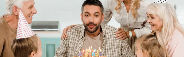 Cropped view of woman touching shoulders of man blowing out candles on birthday cake, panoramic shot — Stock Photo