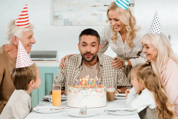 Mulher alegre tocando ombros de homem soprando velas no bolo de aniversário — Fotografia de Stock