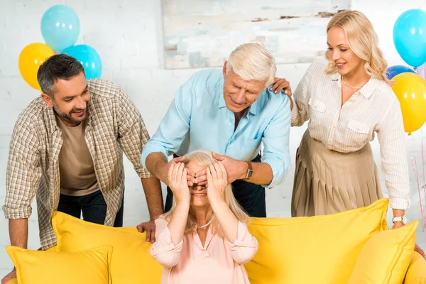 Senior man covering eyes of wife with hands while standing near adult son and daughter — Stock Photo