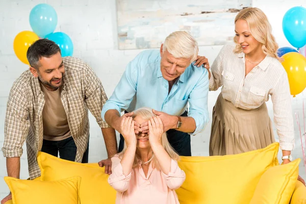 Senior homme couvrant les yeux de la femme avec les mains tout en se tenant près adulte fils et fille — Photo de stock